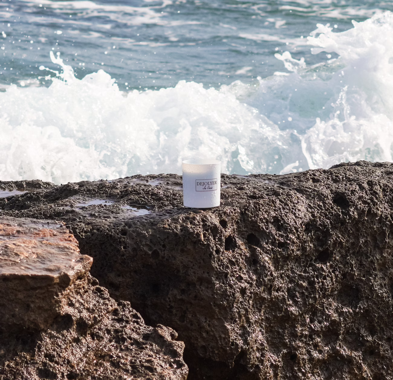 vela perfumada dejolyer en las rocas y la ola rompiendo de fondo