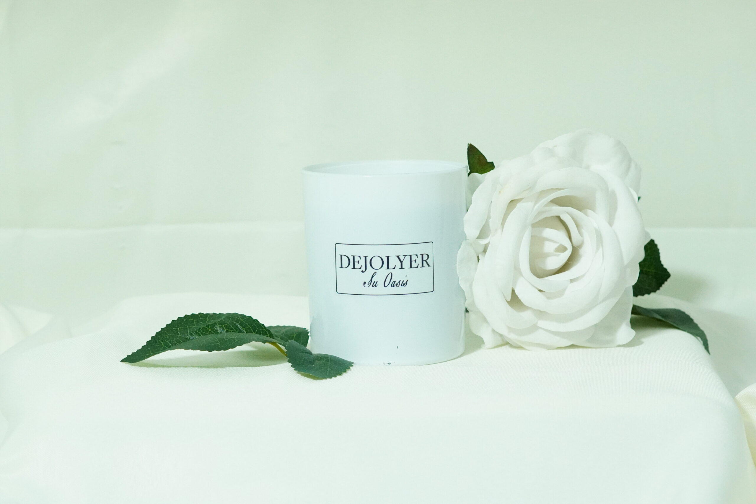 perfume en vela dejolyer sobre una tela blanca y rodeado de una rosa imagen inspiracional su oasis de inspiracion